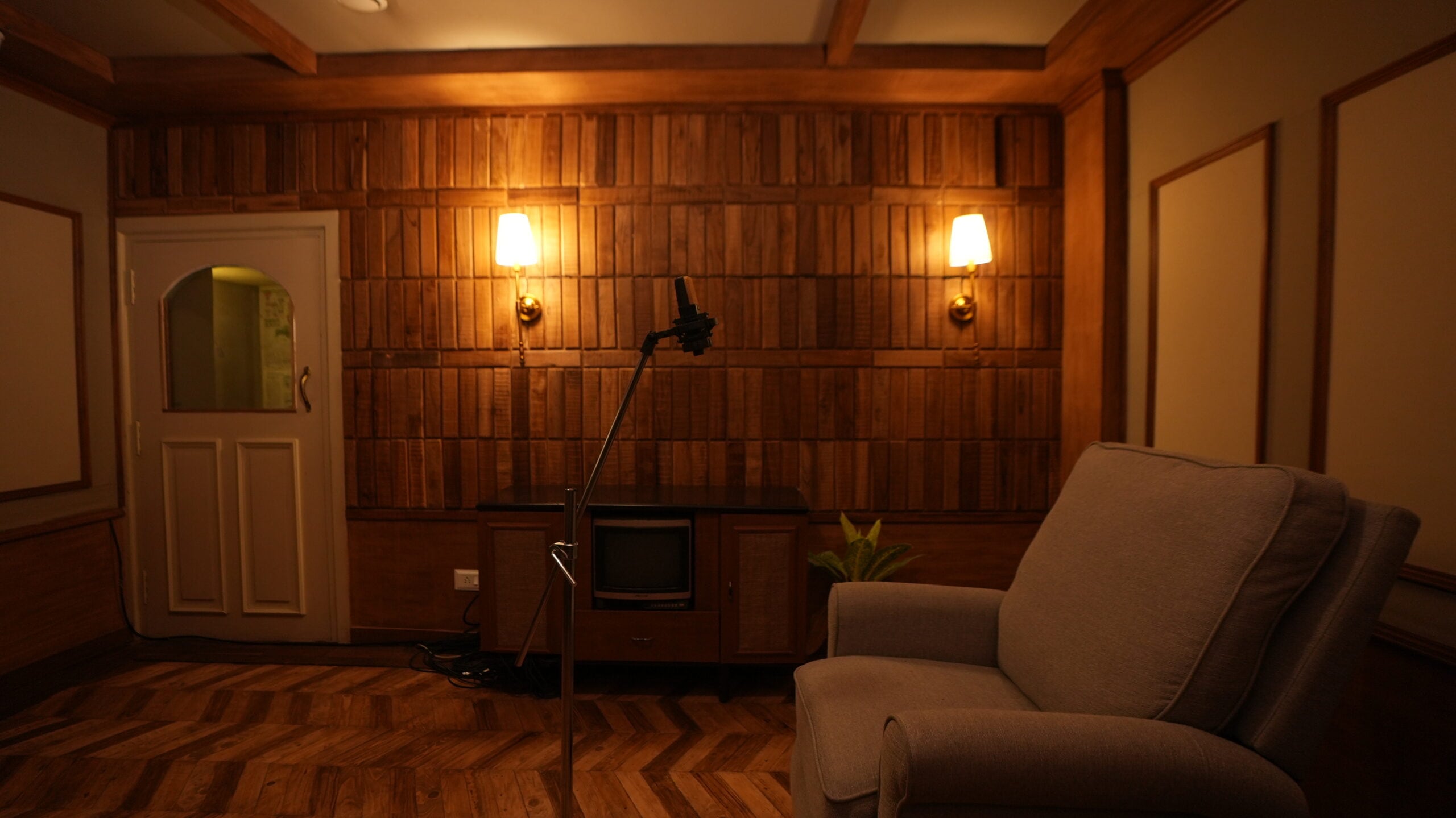 Teak-panelled dubbing room with a microphone and a vintage television, lit by two brass sconces