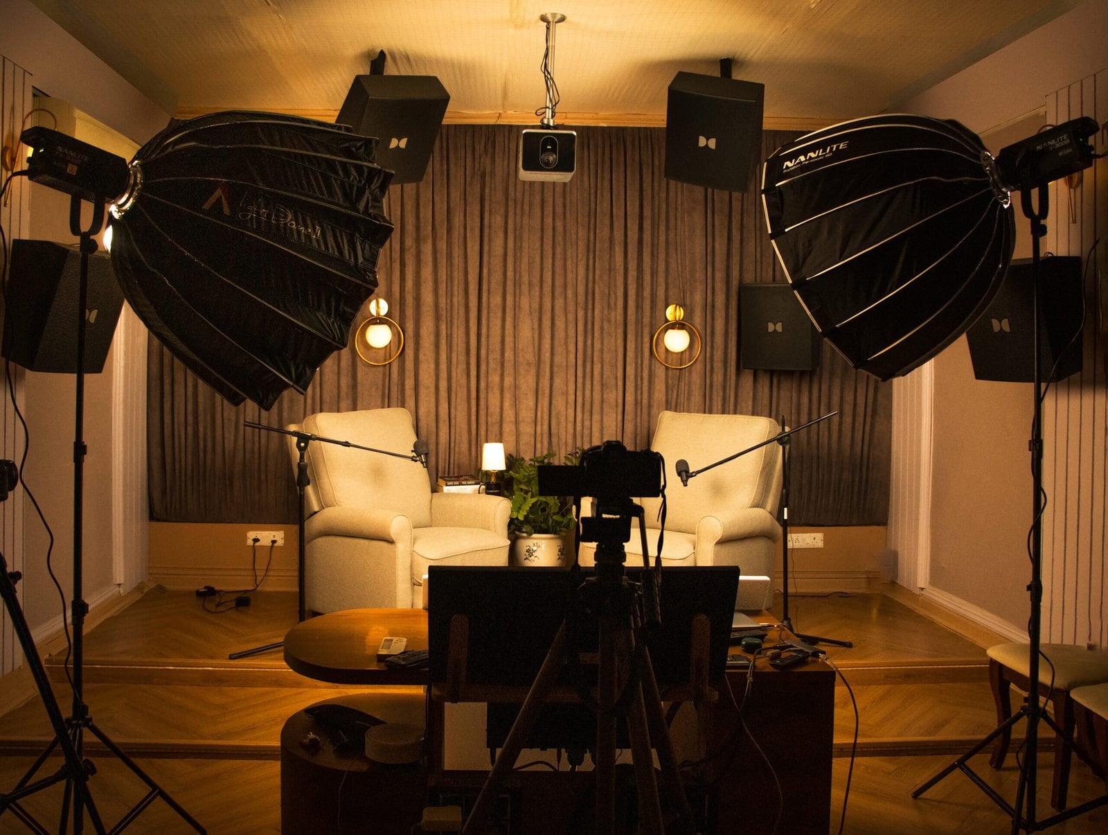 The podcast set lit and ready: two cream armchairs on a platform between boom microphones, with large softboxes either side and Dolby speakers on the walls